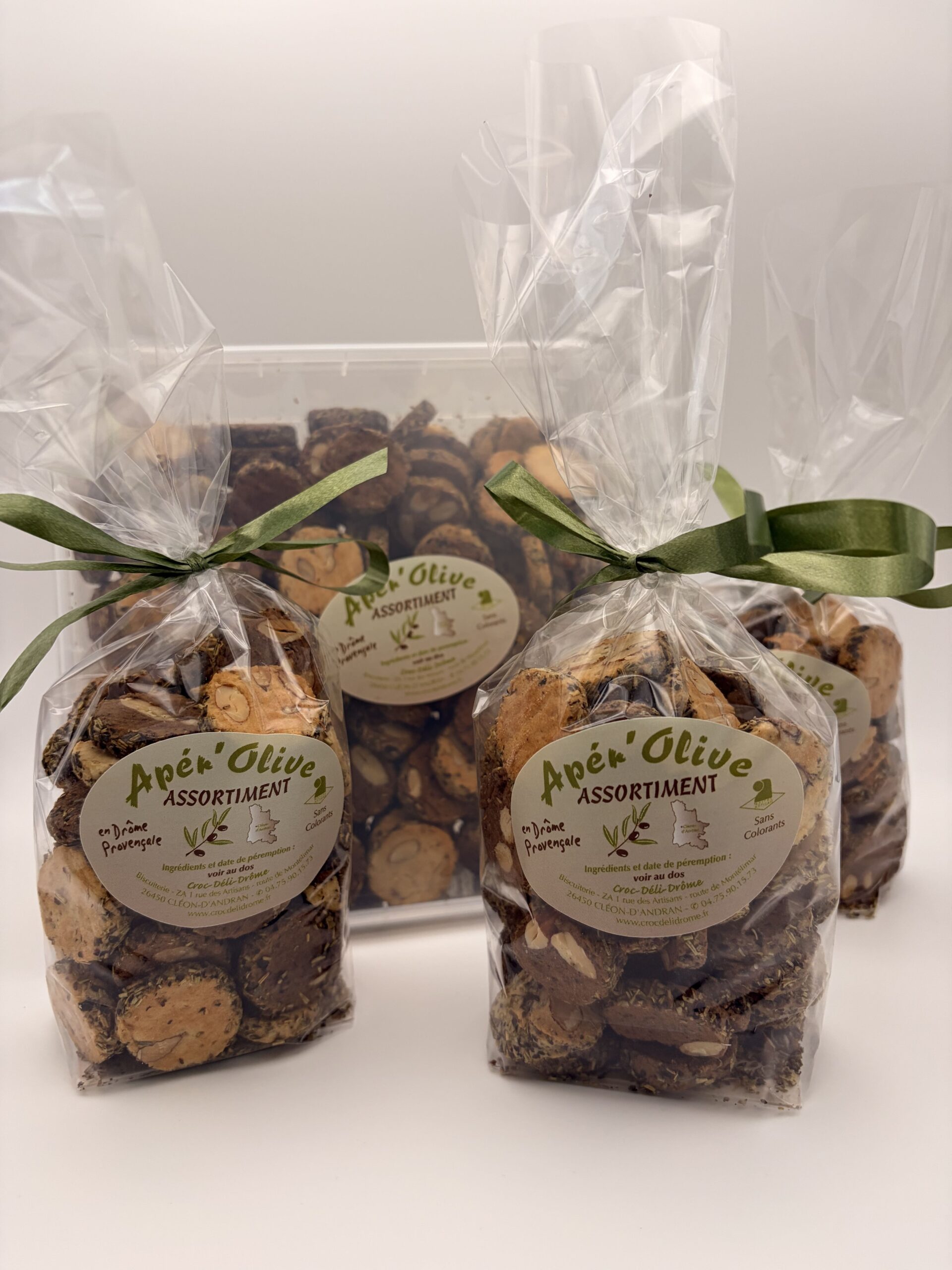 Présentation des différents formats des sablés apéritifs artisanaux Apér'olive Croc'Déli Drôme, montrant trois sachets de 200g avec ruban vert au premier plan et la grande boîte de 650g à l'arrière-plan.