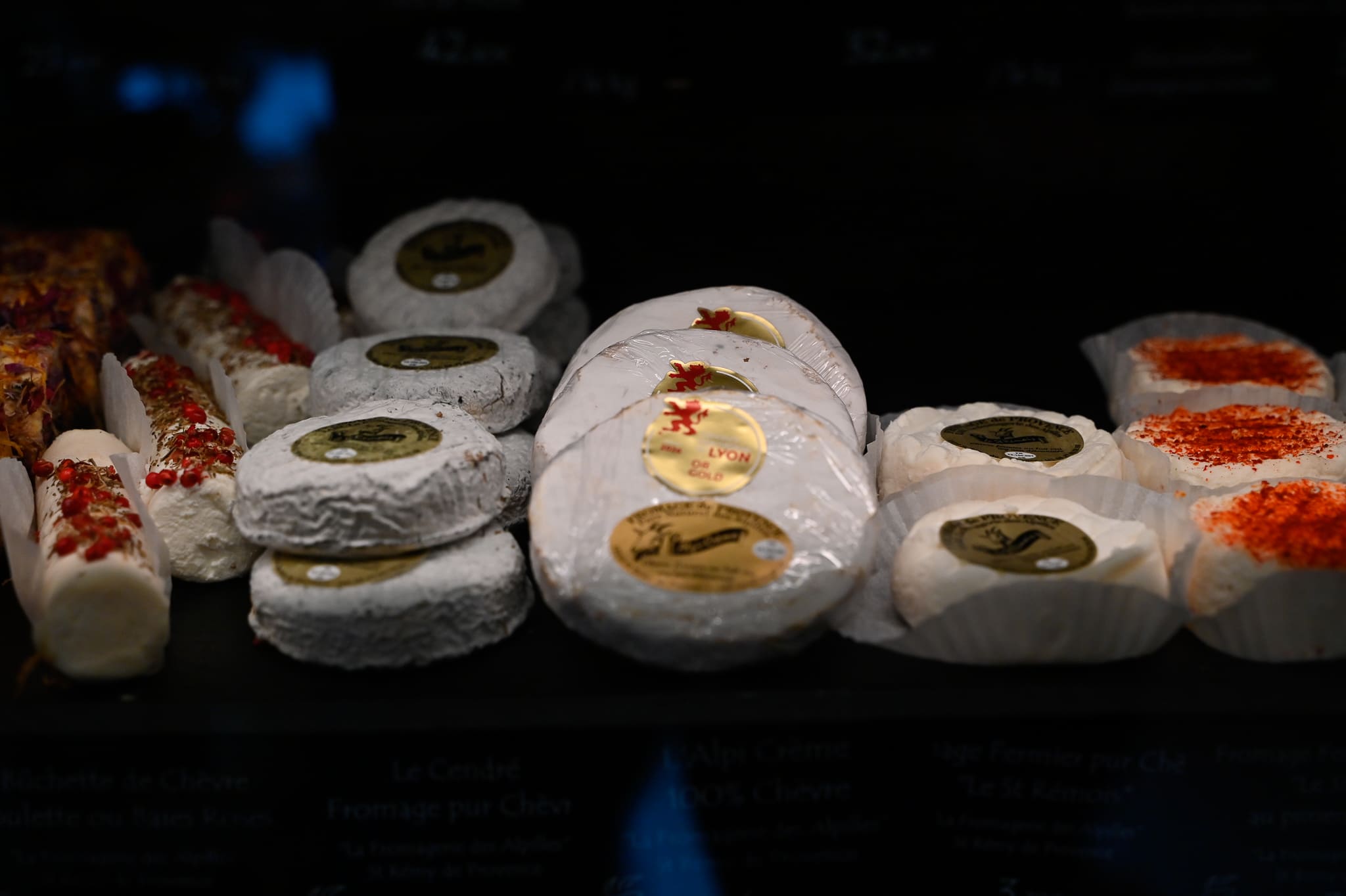 Nos spécialités traiteurs, une sélection de fromages de chèvre artisanaux dans la vitrine de l'épicerie Chez Karen à Saint-Rémy-de-Provence, présentant des bûchettes aux baies roses, des chèvres cendrés et le fromage fermier local "Le St Rémois"