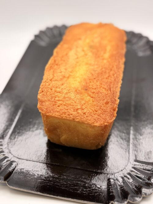 Cake au citron doré présenté entier sur un plateau noir, mettant en valeur sa croûte légèrement croustillante et sa texture moelleuse.