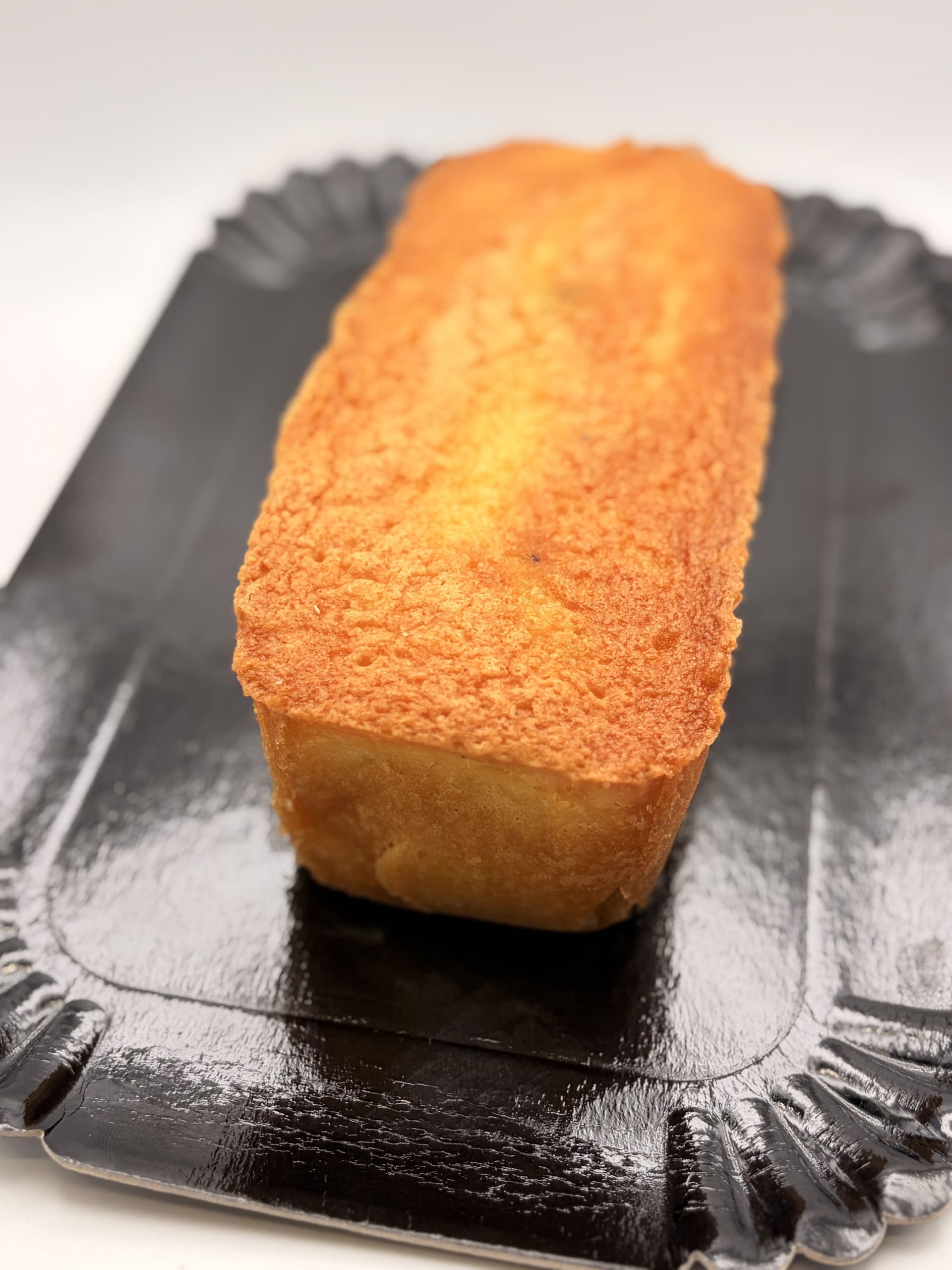 Cake au citron doré présenté entier sur un plateau noir, mettant en valeur sa croûte légèrement croustillante et sa texture moelleuse.