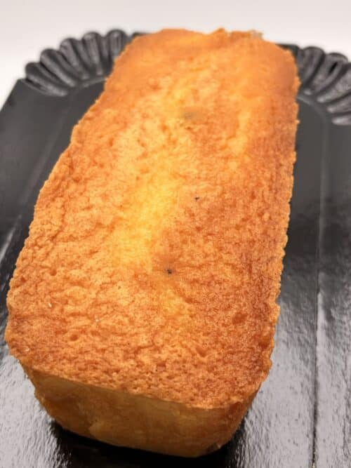Cake au citron entier à la croûte dorée et légèrement croustillante, présenté sur un plateau noir mettant en valeur sa texture moelleuse.