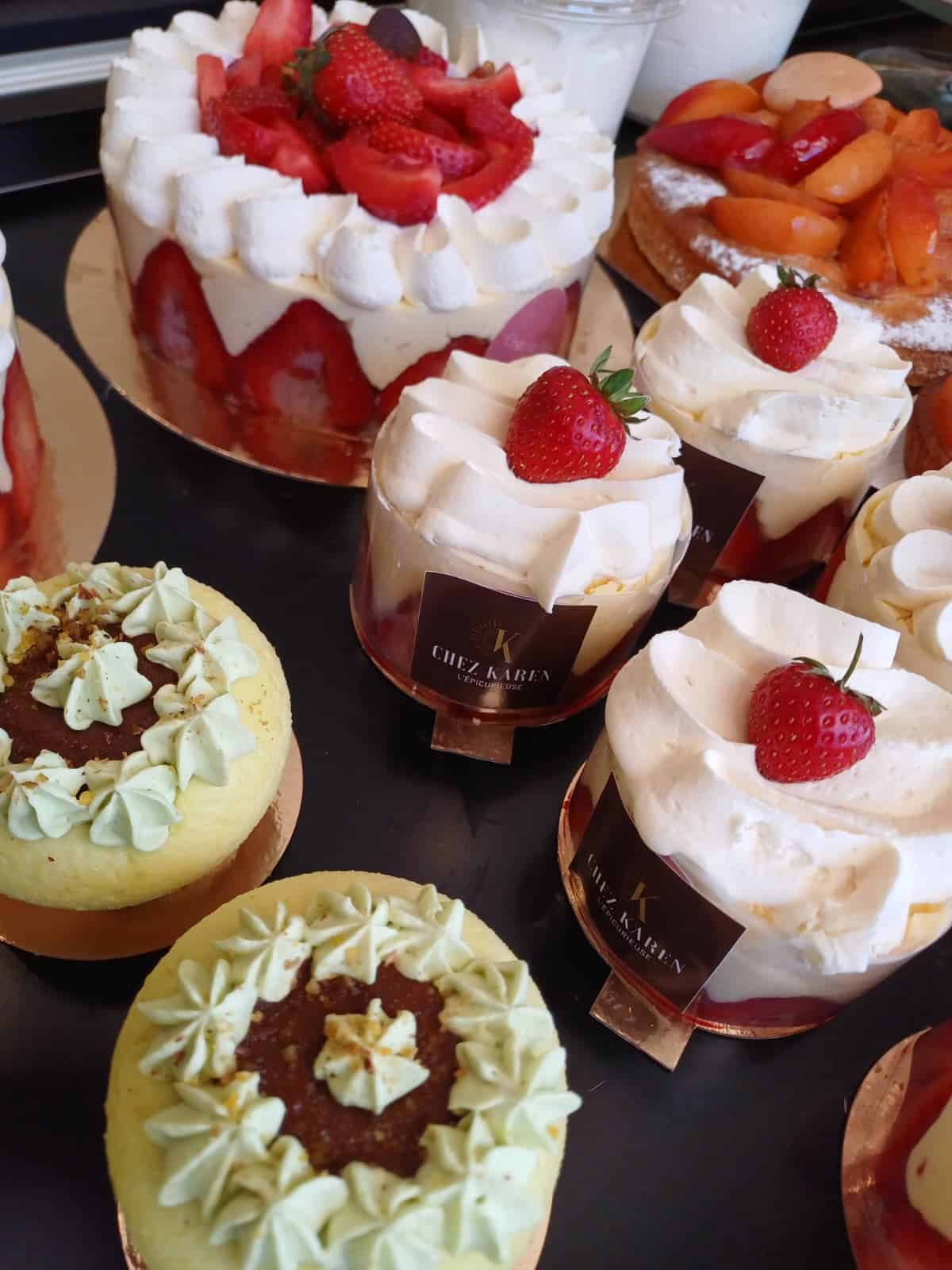 Vue de dessus de plusieurs desserts individuels : des verrines de fraisiers avec crème fouettée et une fraise entière, et des tartelettes à la pistache avec ganache au chocolat et pépites.