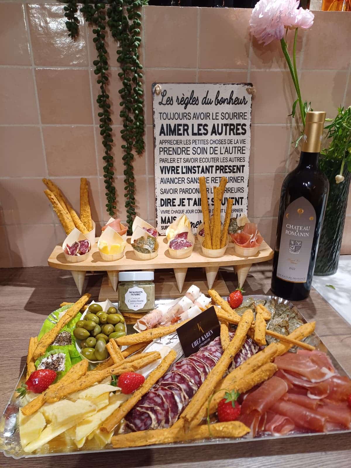 Grand plateau traiteur composé de charcuteries fines, jambon cru, saucisson, fromages, olives vertes, gressins et fraises fraîches, à côté d'une bouteille de vin Château Romanin.