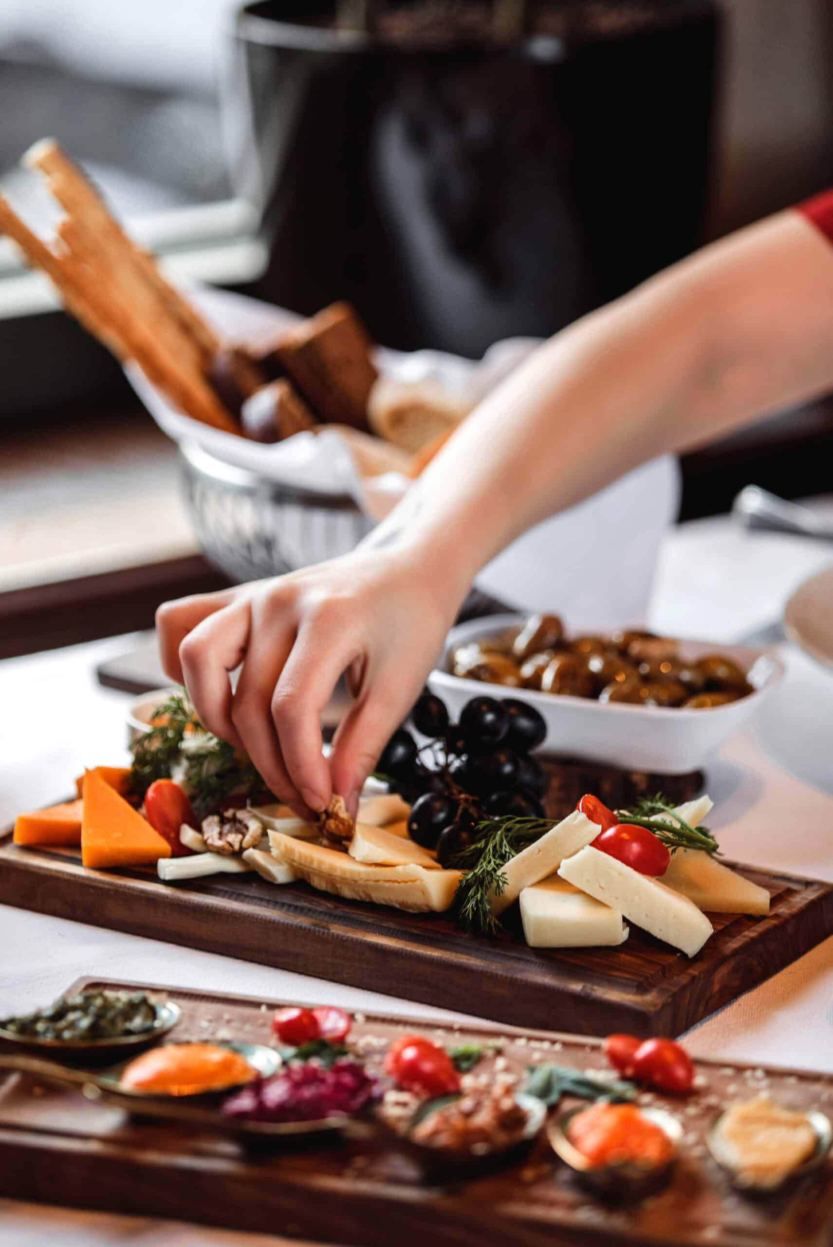 Personne composant un plateau de fromages, raisins, olives et noix lors de la préparation d'un évènement traiteur avec une présentation soignée de produits gourmands.